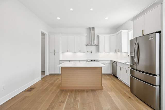 kitchen featuring appliances with stainless steel finishes, wall chimney exhaust hood, light hardwood / wood-style flooring, a center island, and white cabinetry