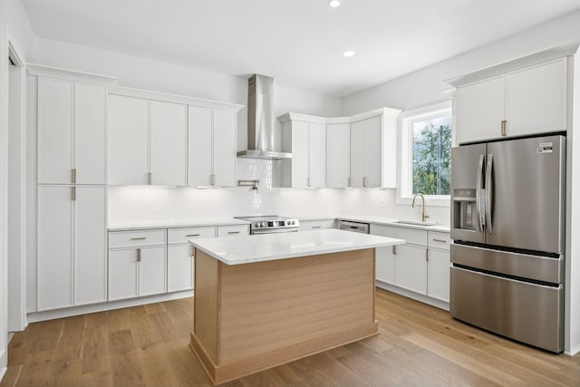 kitchen with appliances with stainless steel finishes, sink, wall chimney range hood, white cabinets, and a center island