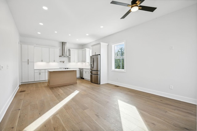 kitchen with wall chimney exhaust hood, light wood-type flooring, appliances with stainless steel finishes, a kitchen island, and white cabinetry