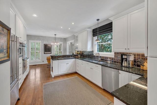 kitchen with appliances with stainless steel finishes, white cabinets, decorative light fixtures, and a peninsula