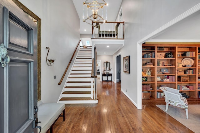 entryway featuring wood-type flooring, a towering ceiling, and an inviting chandelier