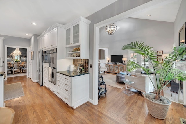 kitchen featuring appliances with stainless steel finishes, tasteful backsplash, an inviting chandelier, light hardwood / wood-style flooring, and white cabinets