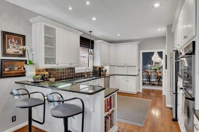 kitchen featuring pendant lighting, glass insert cabinets, white cabinetry, a sink, and a peninsula