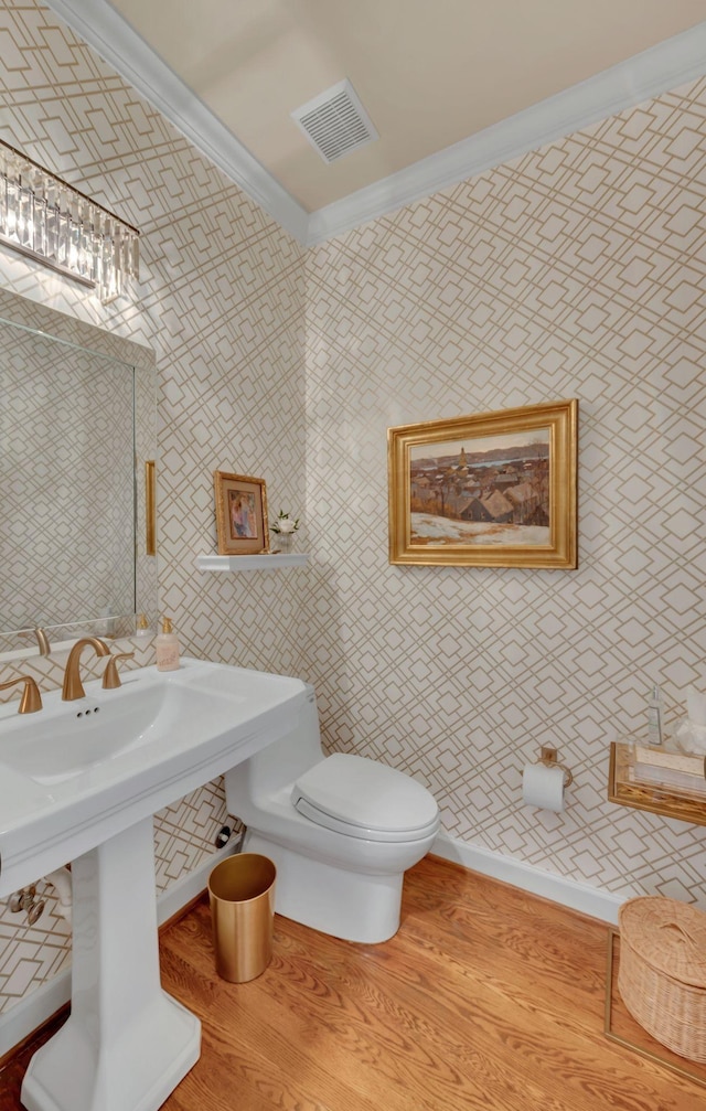 bathroom featuring baseboards, visible vents, toilet, ornamental molding, and wood finished floors