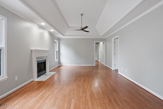 unfurnished living room featuring a tray ceiling, a premium fireplace, crown molding, and ceiling fan