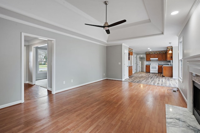 unfurnished living room featuring light wood-type flooring, a tray ceiling, ceiling fan, crown molding, and a premium fireplace