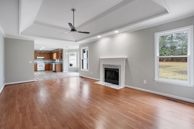 unfurnished living room featuring crown molding, ceiling fan, a fireplace, a tray ceiling, and light hardwood / wood-style floors