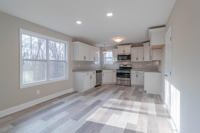 kitchen with white cabinets, decorative light fixtures, light stone counters, and appliances with stainless steel finishes