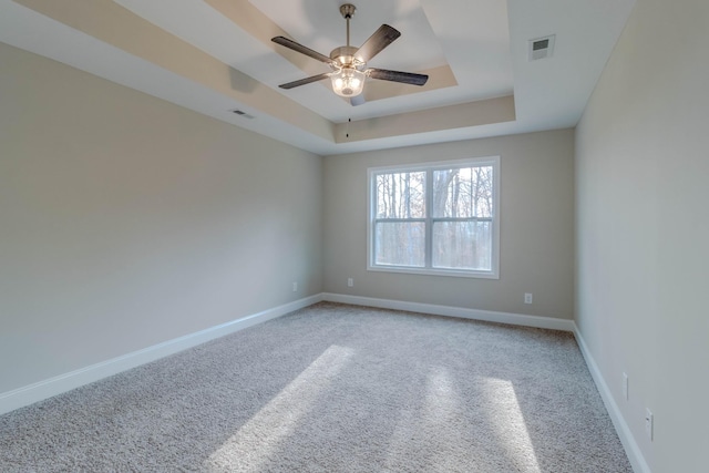 carpeted spare room with a tray ceiling and ceiling fan