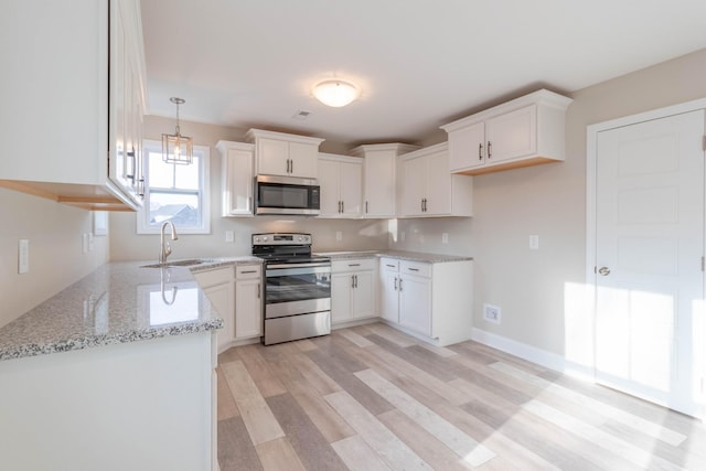 kitchen with sink, hanging light fixtures, appliances with stainless steel finishes, white cabinets, and light wood-type flooring