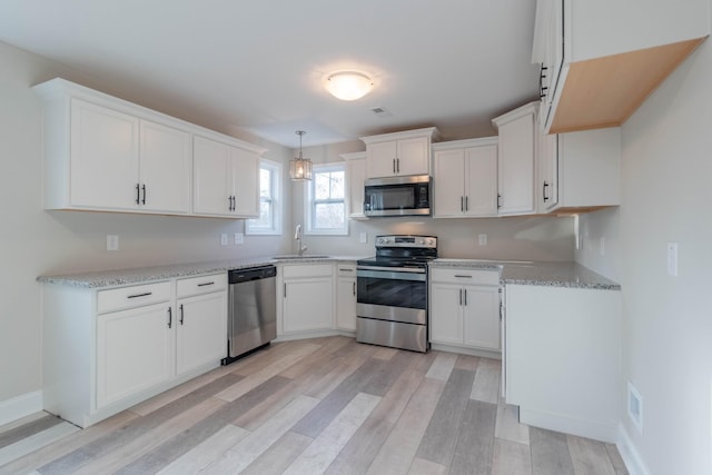 kitchen featuring light wood-type flooring, stainless steel appliances, sink, decorative light fixtures, and white cabinets