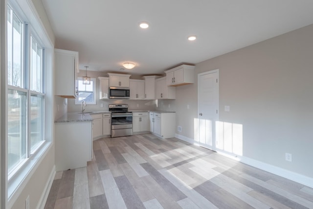 kitchen with white cabinetry, sink, light stone counters, light hardwood / wood-style floors, and appliances with stainless steel finishes