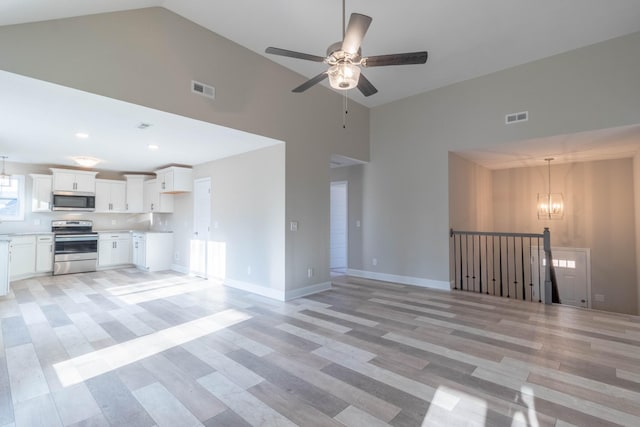 unfurnished living room with high vaulted ceiling, light hardwood / wood-style floors, and ceiling fan with notable chandelier