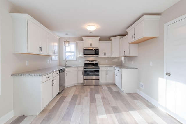 kitchen with white cabinetry, sink, light stone countertops, hanging light fixtures, and appliances with stainless steel finishes