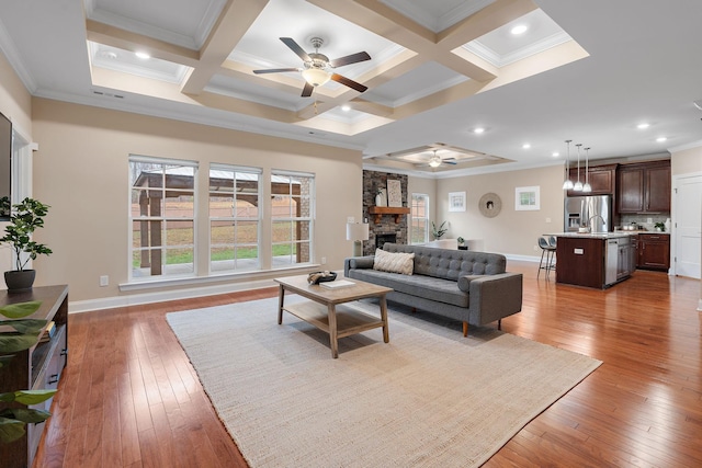 living room featuring ceiling fan, crown molding, a fireplace, and coffered ceiling