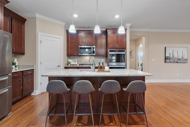 kitchen with hanging light fixtures, light stone counters, a center island with sink, and stainless steel appliances