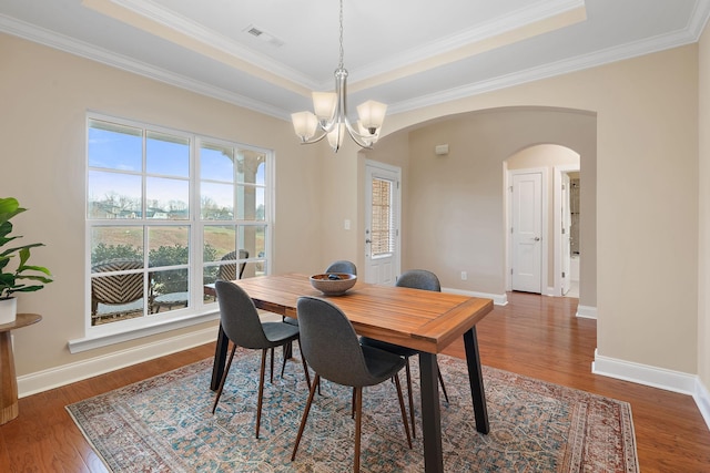 dining area with a tray ceiling, crown molding, dark hardwood / wood-style flooring, and an inviting chandelier