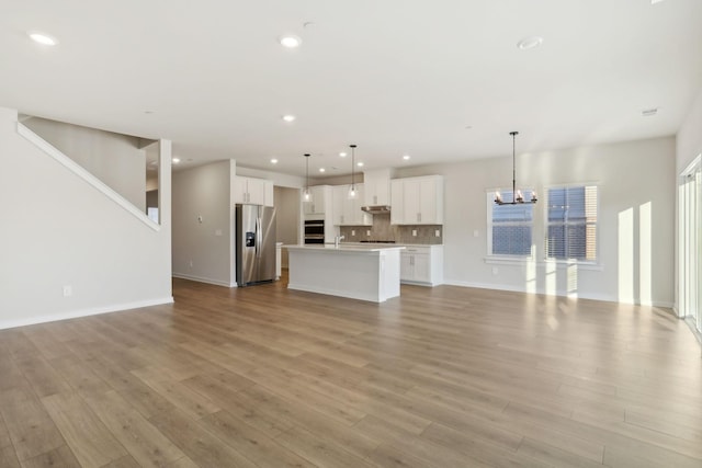 unfurnished living room featuring recessed lighting, a chandelier, a sink, and light wood finished floors