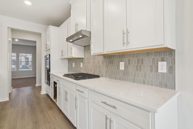 kitchen with under cabinet range hood, white cabinets, decorative backsplash, baseboards, and stainless steel gas cooktop