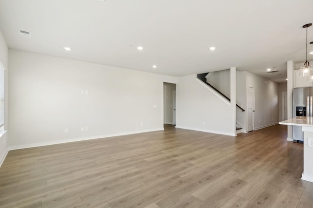 unfurnished living room featuring light wood finished floors, recessed lighting, stairs, and baseboards