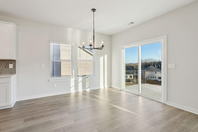 unfurnished dining area featuring light wood-style flooring, a notable chandelier, baseboards, and visible vents