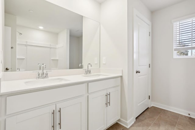 bathroom with double vanity, a shower, baseboards, and a sink