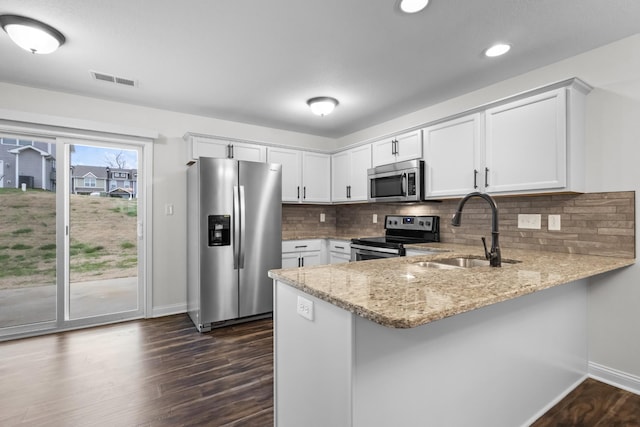 kitchen with kitchen peninsula, decorative backsplash, stainless steel appliances, sink, and white cabinetry