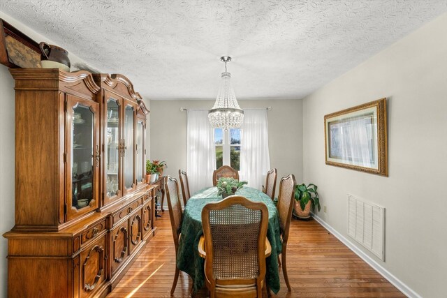 dining area with hardwood / wood-style floors, a notable chandelier, and a textured ceiling