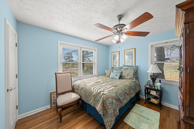 bedroom with ceiling fan, dark hardwood / wood-style floors, a textured ceiling, and multiple windows