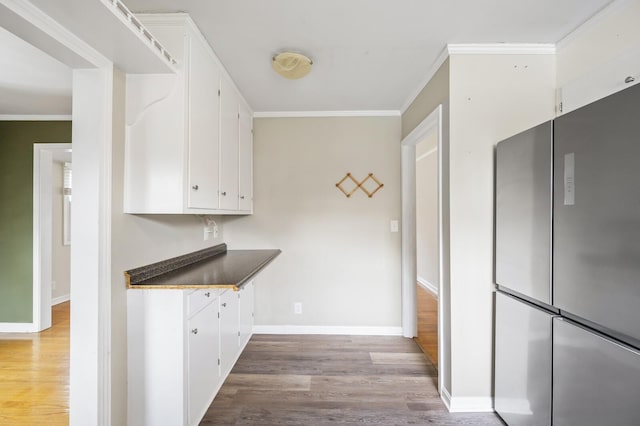 kitchen with hardwood / wood-style floors, white cabinetry, stainless steel refrigerator, and crown molding