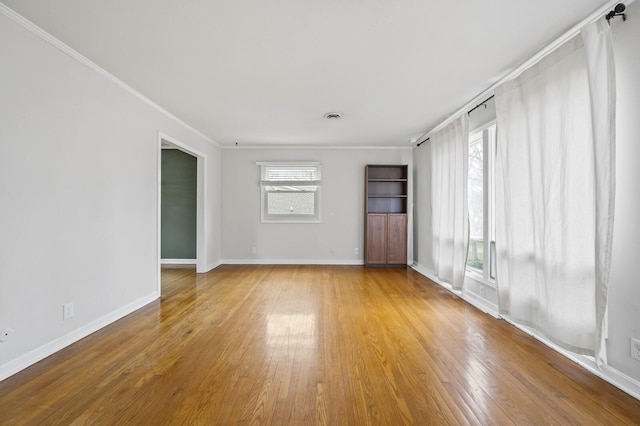 empty room with a wealth of natural light, crown molding, and light hardwood / wood-style floors