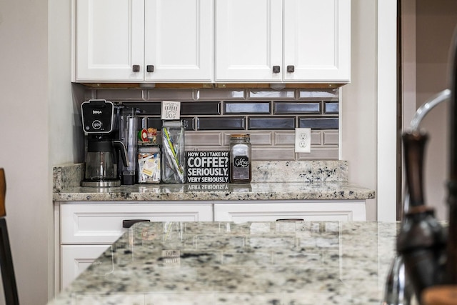 bar with white cabinets, tasteful backsplash, and light stone countertops