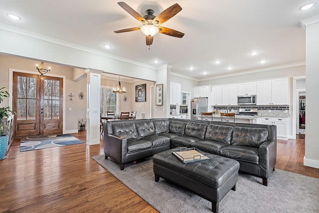 living room with decorative columns, ornamental molding, ceiling fan with notable chandelier, and hardwood / wood-style flooring