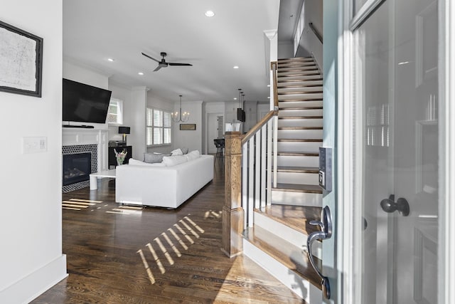 stairway featuring ceiling fan with notable chandelier, wood-type flooring, a tile fireplace, and crown molding