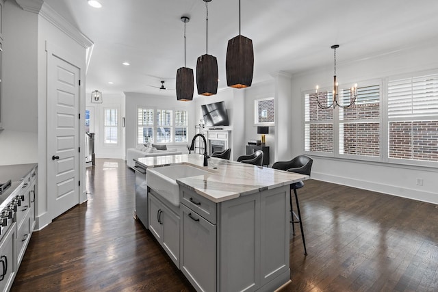 kitchen with decorative light fixtures, gray cabinetry, light stone countertops, a breakfast bar, and an island with sink