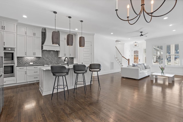 kitchen featuring custom exhaust hood, decorative light fixtures, decorative backsplash, a kitchen island with sink, and a breakfast bar area