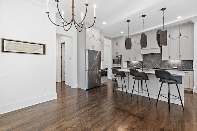 kitchen featuring custom exhaust hood, appliances with stainless steel finishes, decorative light fixtures, a breakfast bar, and a center island with sink