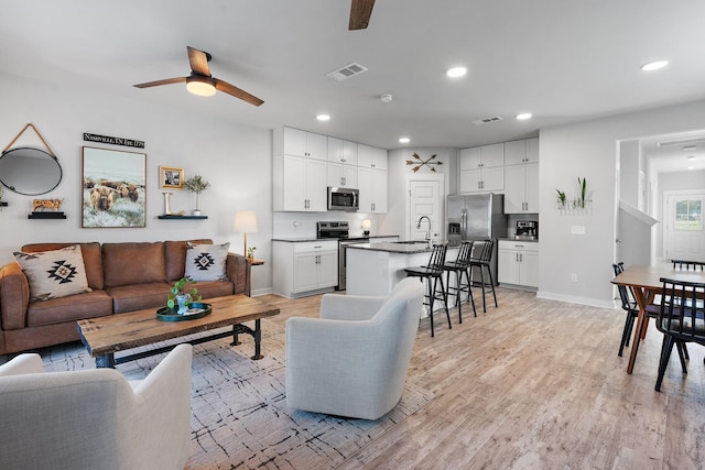 living room with ceiling fan, light wood-type flooring, and sink