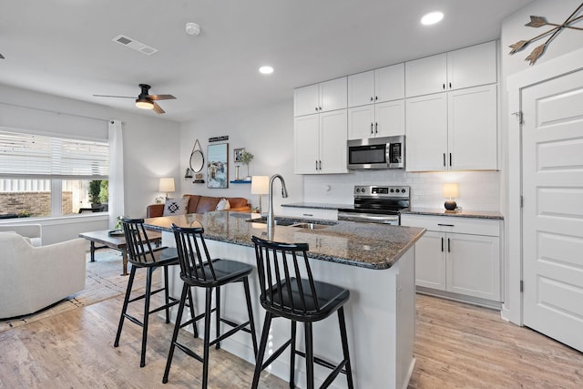 kitchen with dark stone counters, white cabinets, sink, an island with sink, and stainless steel appliances