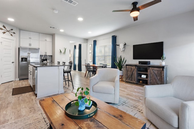 living room with light hardwood / wood-style flooring, ceiling fan, and sink