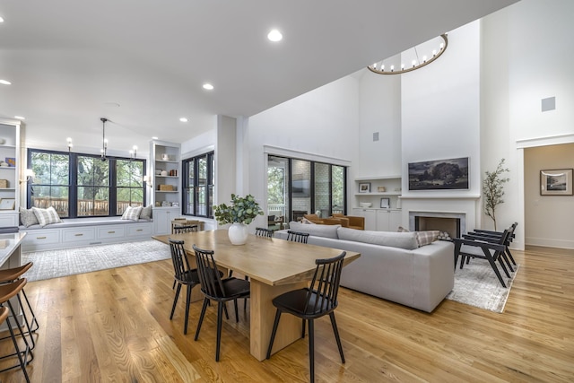 dining room with light hardwood / wood-style flooring, built in features, a chandelier, and a high ceiling