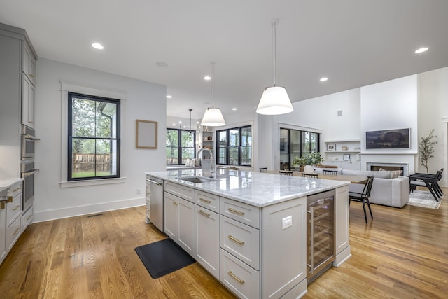 kitchen with sink, a kitchen island with sink, hanging light fixtures, wine cooler, and light stone counters