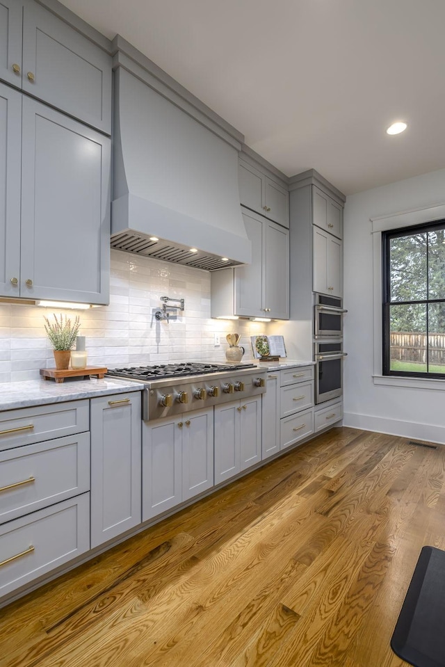 kitchen with tasteful backsplash, gray cabinetry, light hardwood / wood-style floors, stainless steel appliances, and custom range hood