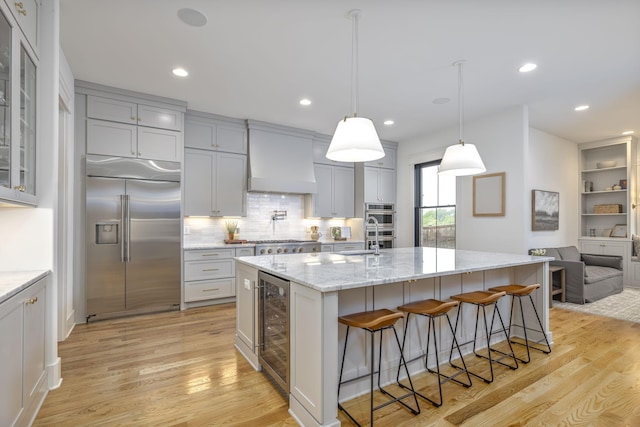 kitchen featuring beverage cooler, a kitchen island with sink, light hardwood / wood-style floors, stainless steel appliances, and custom range hood