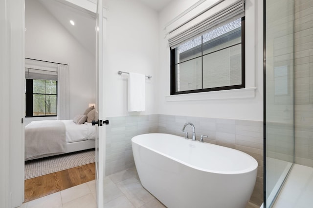 bathroom featuring tile patterned floors, vaulted ceiling, tile walls, and a washtub