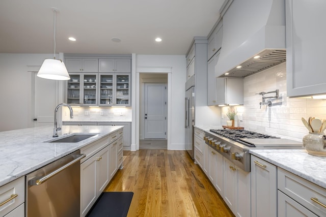 kitchen with sink, custom exhaust hood, light stone counters, pendant lighting, and stainless steel appliances