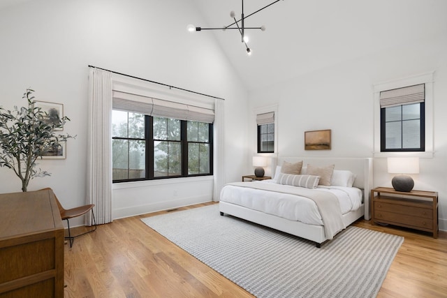 bedroom featuring high vaulted ceiling, a chandelier, and light wood-type flooring