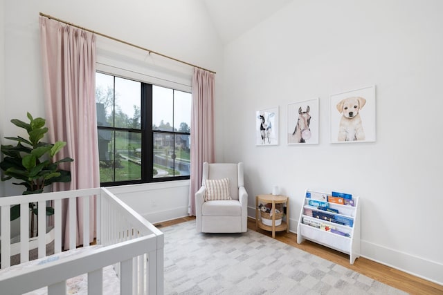 bedroom with a nursery area, light hardwood / wood-style floors, and vaulted ceiling