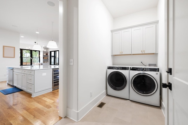 washroom with wine cooler, sink, washing machine and dryer, cabinets, and light hardwood / wood-style floors