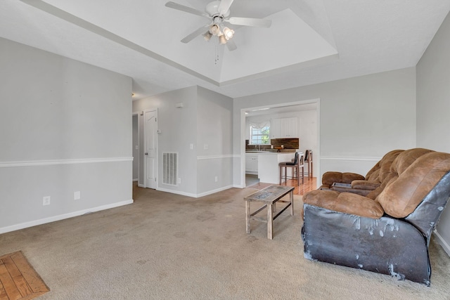 carpeted living room featuring a raised ceiling, ceiling fan, and sink